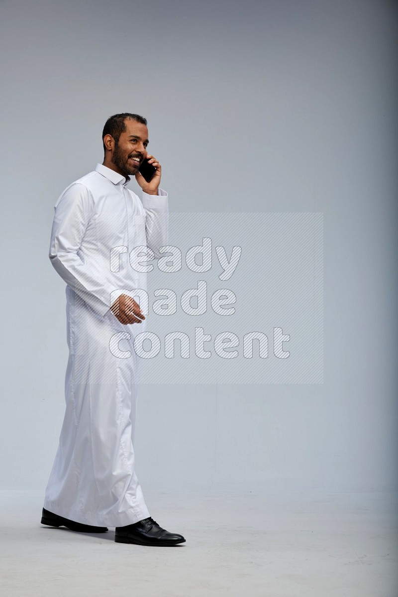 Saudi man wearing Thob standing talking on phone on Gray background