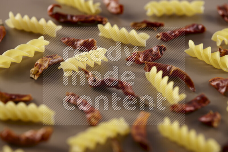 Raw pasta with different ingredients such as cherry tomatoes, garlic, onions, red chilis, black pepper, white pepper, bay laurel leaves, rosemary and cardamom on beige background