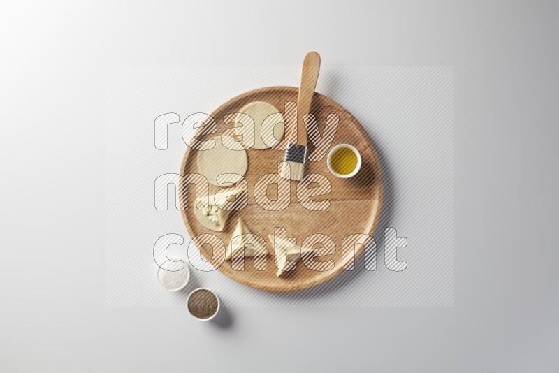 two closed sambosas and one open sambosa filled with cheese while salt, black pepper and oil with oil brush aside in a wooden dish on a white background