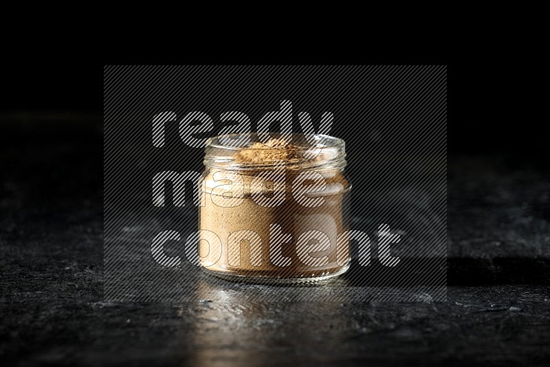 A glass jar full of allspice powder on a textured black flooring