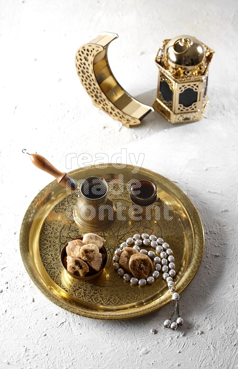 Dried figs in a metal bowl with coffee and prayer beads on a tray beside lanterns in a light setup