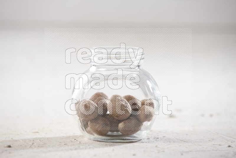 A glass spice jar full of whole nutmeg seeds on a textured white flooring