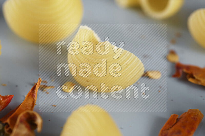 Raw pasta with different ingredients such as cherry tomatoes, garlic, onions, red chilis, black pepper, white pepper, bay laurel leaves, rosemary, cardamom and mushrooms on light blue background