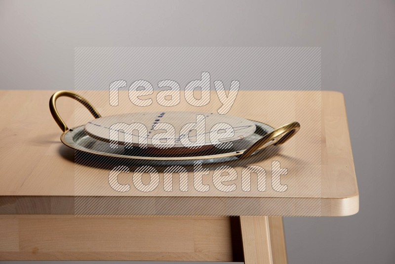 multicolored plate placed on a rounded stainless steel tray with golden handels on the edge of wooden table