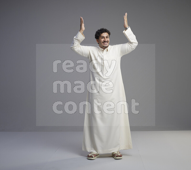 A Saudi man standing wearing thob interacting with the camera on gray background