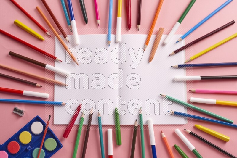 A blank open notebook with coloring pens on rose background