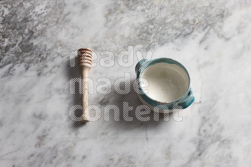 Multicolored pottery bowl with wooden honey dipper on the side on grey marble background