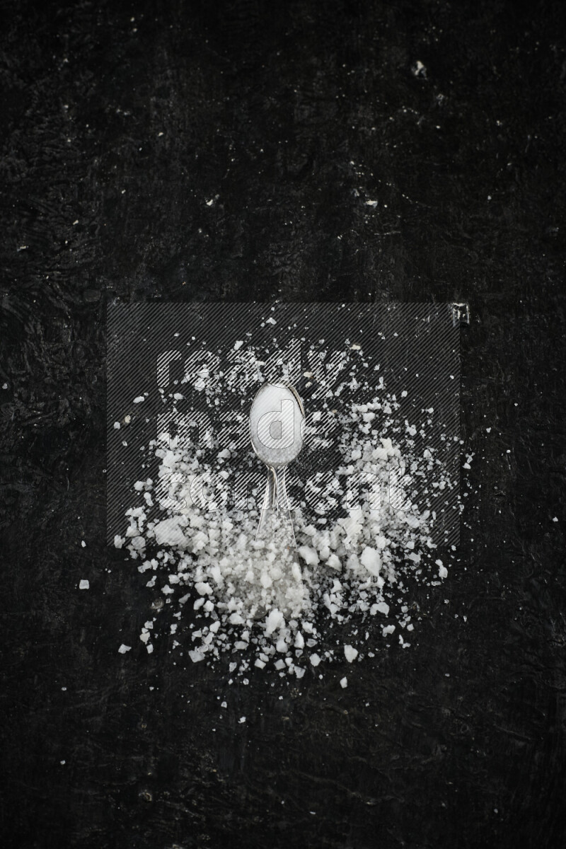 ملعقتان معدنيتان ممتلئتان بالملح الأبيض على خلفية سوداء