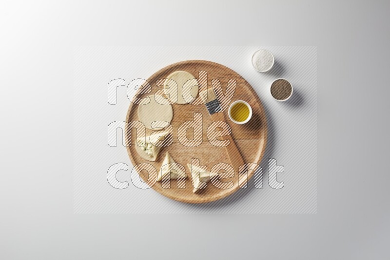 two closed sambosas and one open sambosa filled with cheese while salt, black pepper and oil with oil brush aside in a wooden dish on a white background