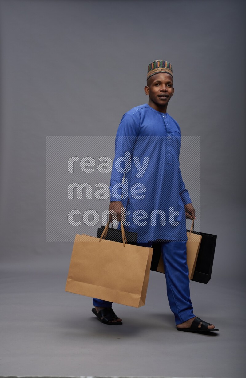 Man wearing Nigerian outfit standing holding shopping bag on gray background