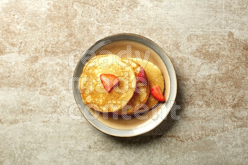 Three stacked strawberry pancakes in a bicolor plate on beige background