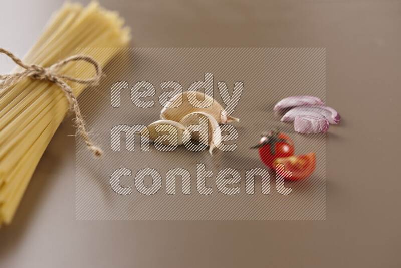 Raw pasta with different ingredients such as cherry tomatoes, garlic, onions, red chilis, black pepper, white pepper, bay laurel leaves, rosemary and cardamom on beige background