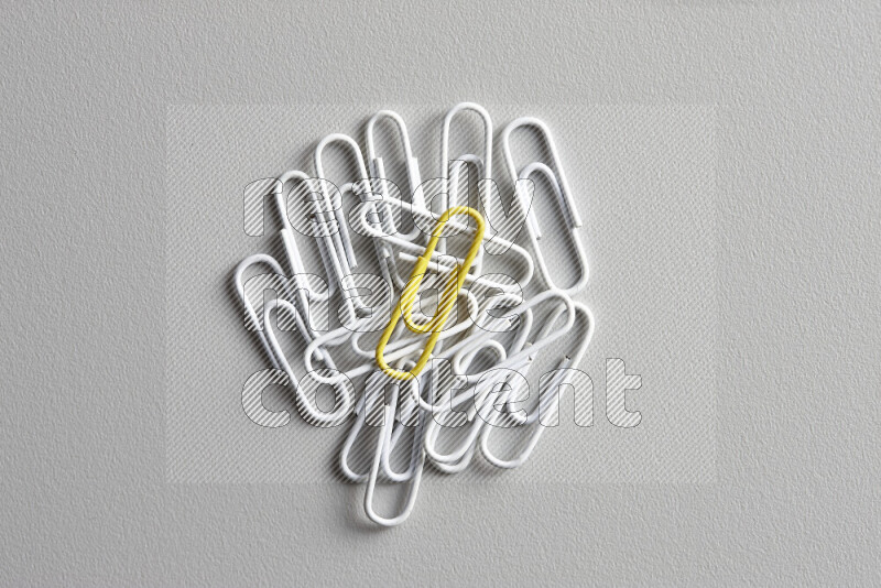 A yellow paperclip surrounded by bunch of white paperclips on grey background