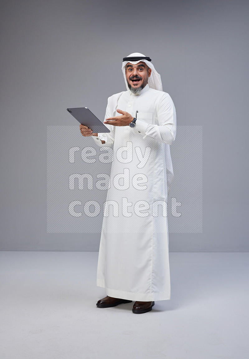 Saudi man Wearing Thob and white Shomag standing working on tablet on Gray background