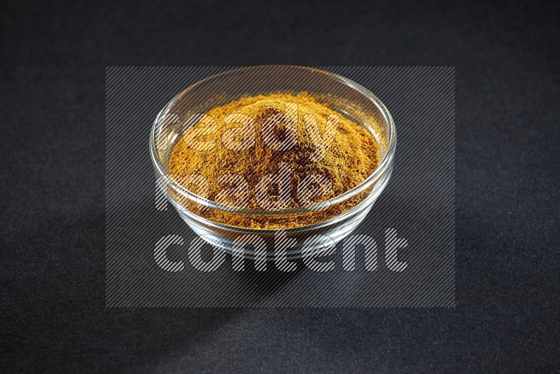A glass bowl full of turmeric powder on black flooring