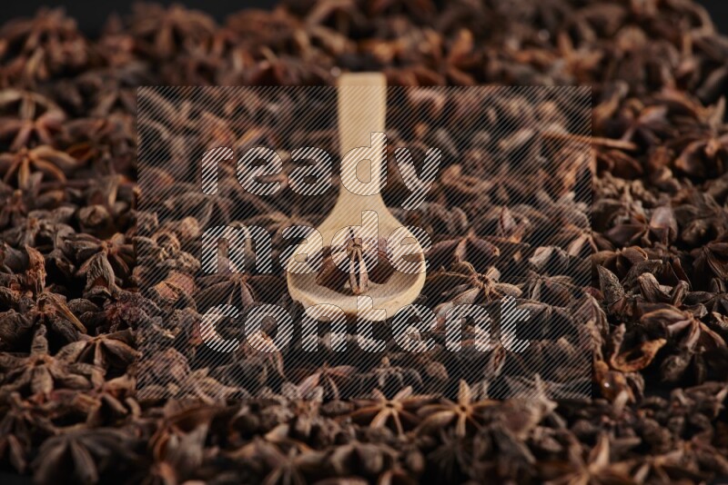Star Anise in a wooden spoon on more stars anise filling the frame on black flooring