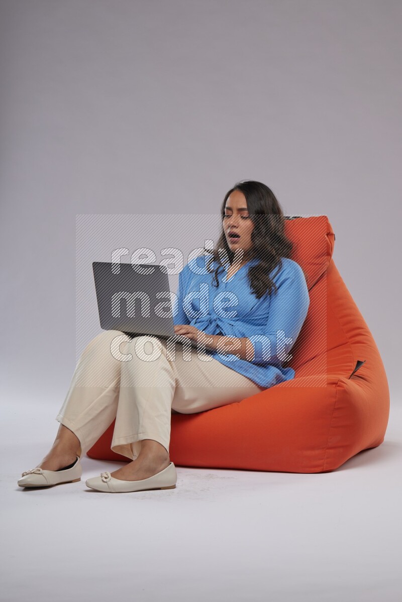 A woman sitting on an orange beanbag and working on laptop
