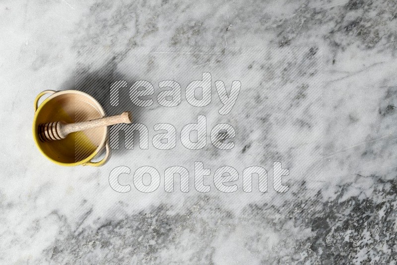 Multicolored Pottery Bowl with wooden honey handle in it, on grey marble flooring, Top View