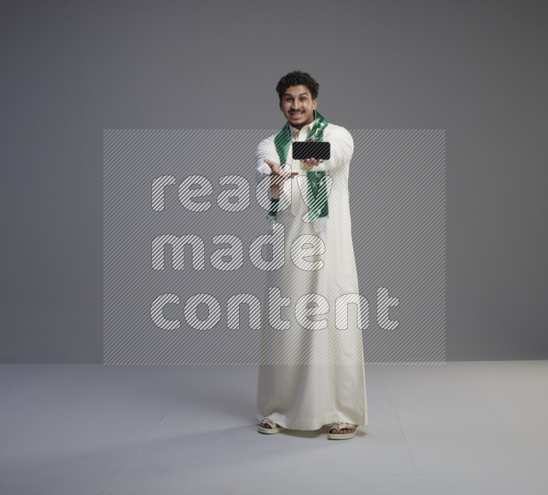 رجل سعودي يرتدي ثوب ابيض و شال يحمل جوال