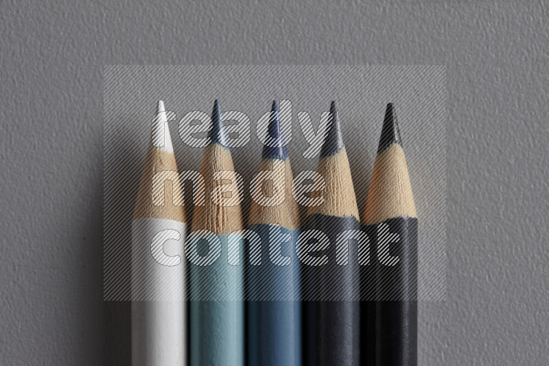 A collection of colored pencils arranged showcasing a gradient of white, grey and black hues on grey background