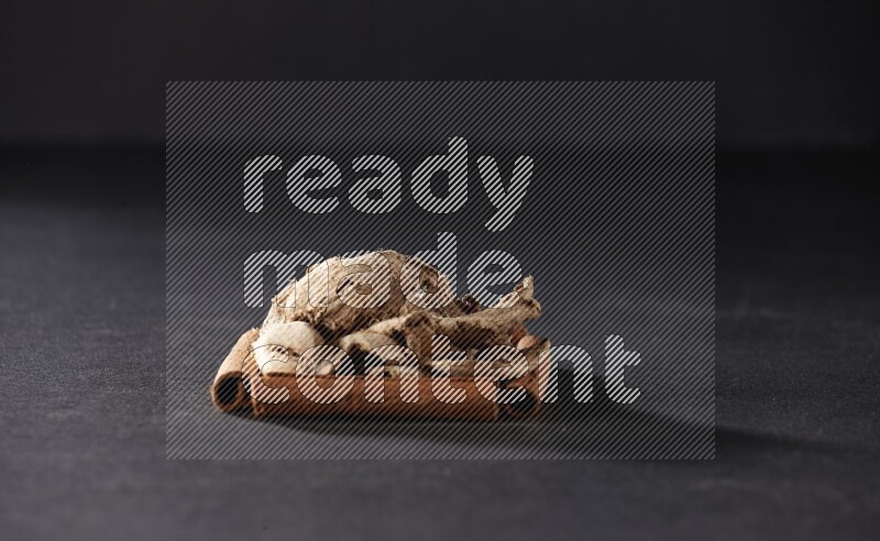 أربعة من أعواد القرفة مكونة شكل مربع بداخلها زنجبيل مجفف علي خلفية سوداء