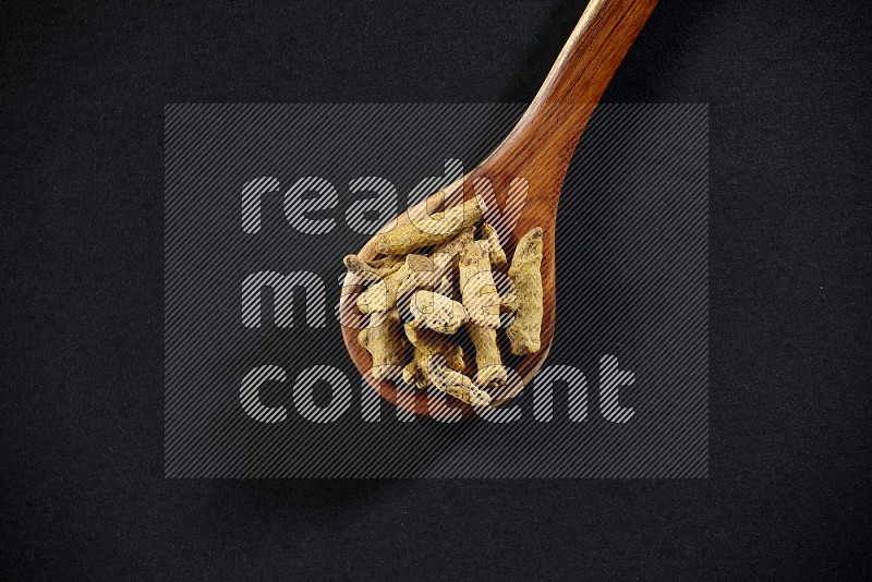 A wooden ladle full of dried turmeric fingers on black flooring