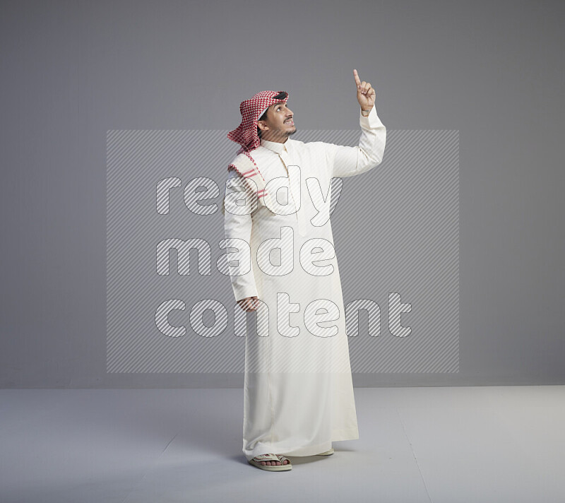 رجل سعودي يرتدي ثوب ابيض وشماغ احمر يشير بيده