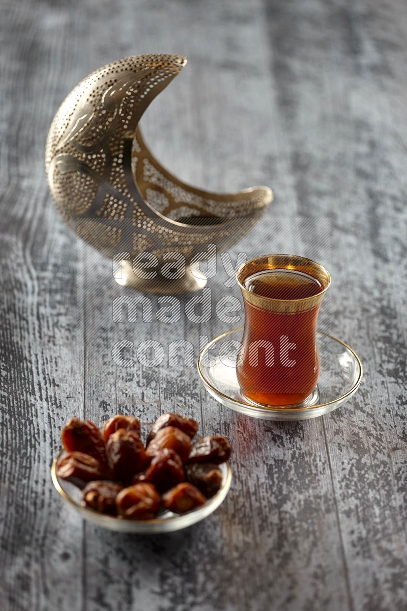 A silver lantern with drinks, dates, nuts, prayer beads and quran on grey wooden background