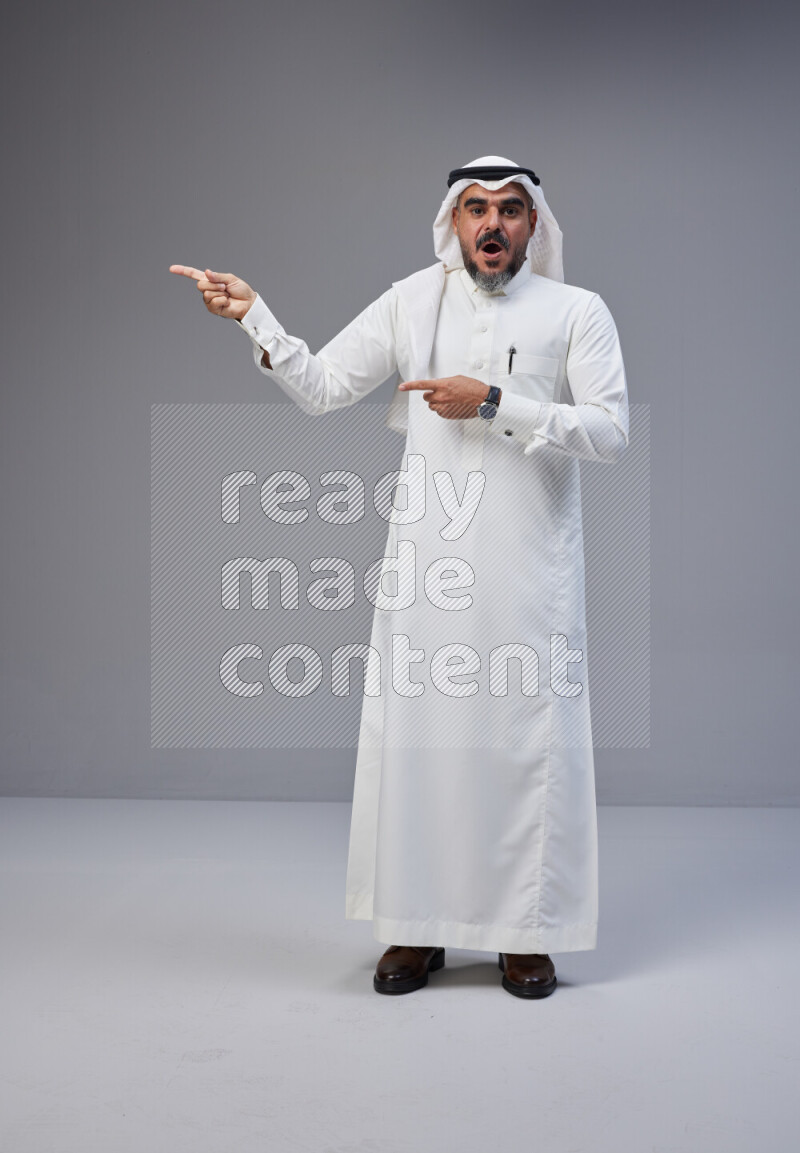 Saudi man Wearing Thob and white Shomag standing interacting with the camera on Gray background