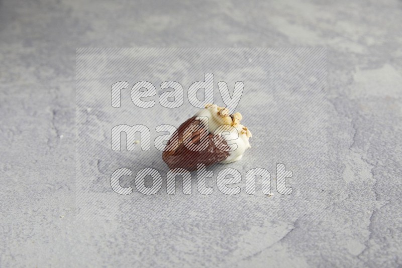 Pecan stuffed date covered with white chocolate and chopped walnuts on alight grey background