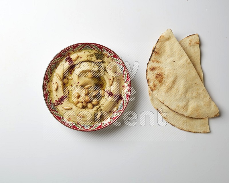 Hummus in a red plate with patterns garnished with zaatar & sumak on a white background