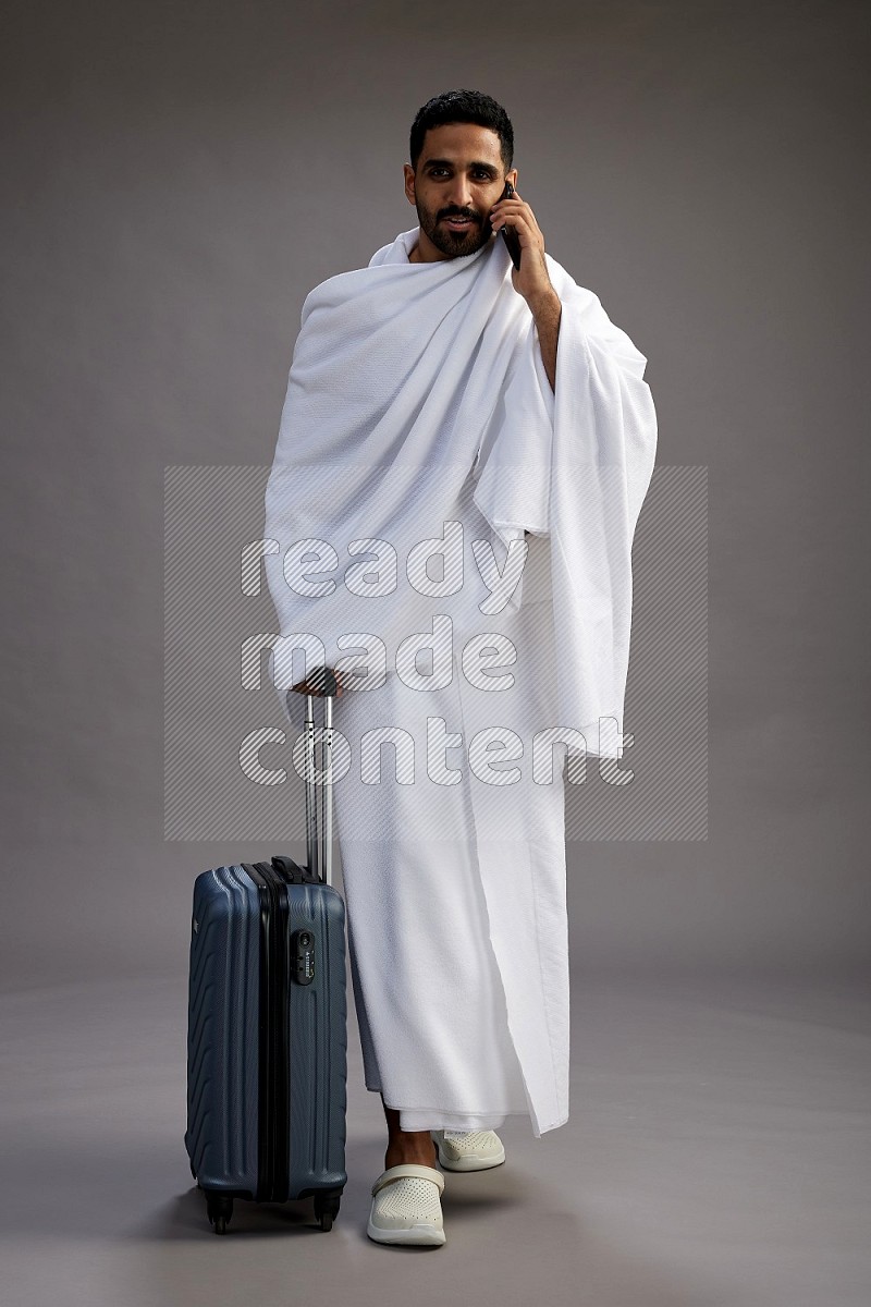 A man wearing Ehram Standing holding traveling bag on gray background