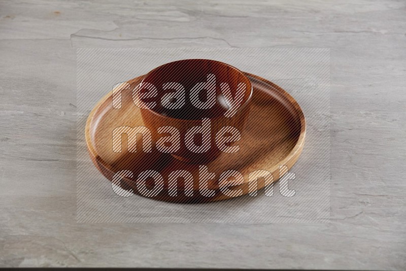 brown wood round bowl on top of brown wood round plate on grey textured countertop