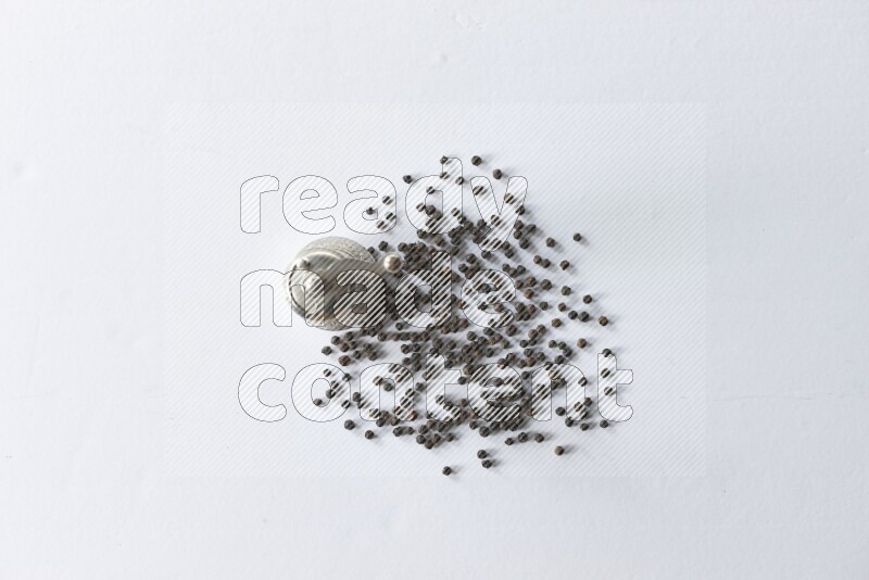 A turkish metal pepper grinder and spreaded black pepper beads on a white flooring