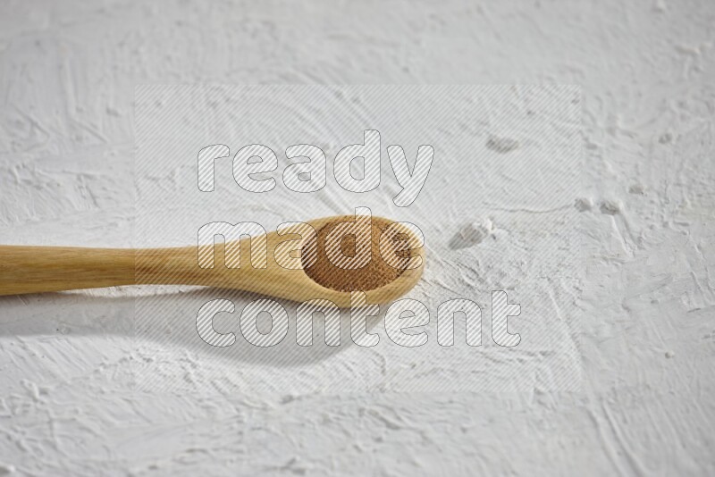 Cinnamon powder in a wooden spoon on a white background