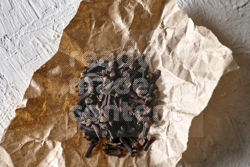 Cloves on crumpled piece of paper on a textured white flooring