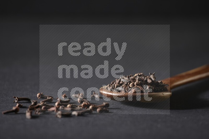 A wooden ladle full of whole cloves on a black flooring