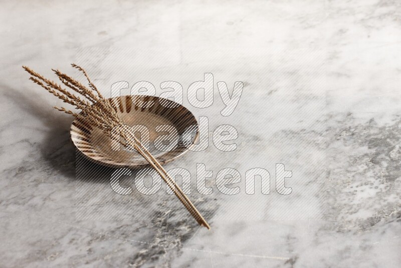 Wheat stalks on multicolored pottery plate on grey marble background