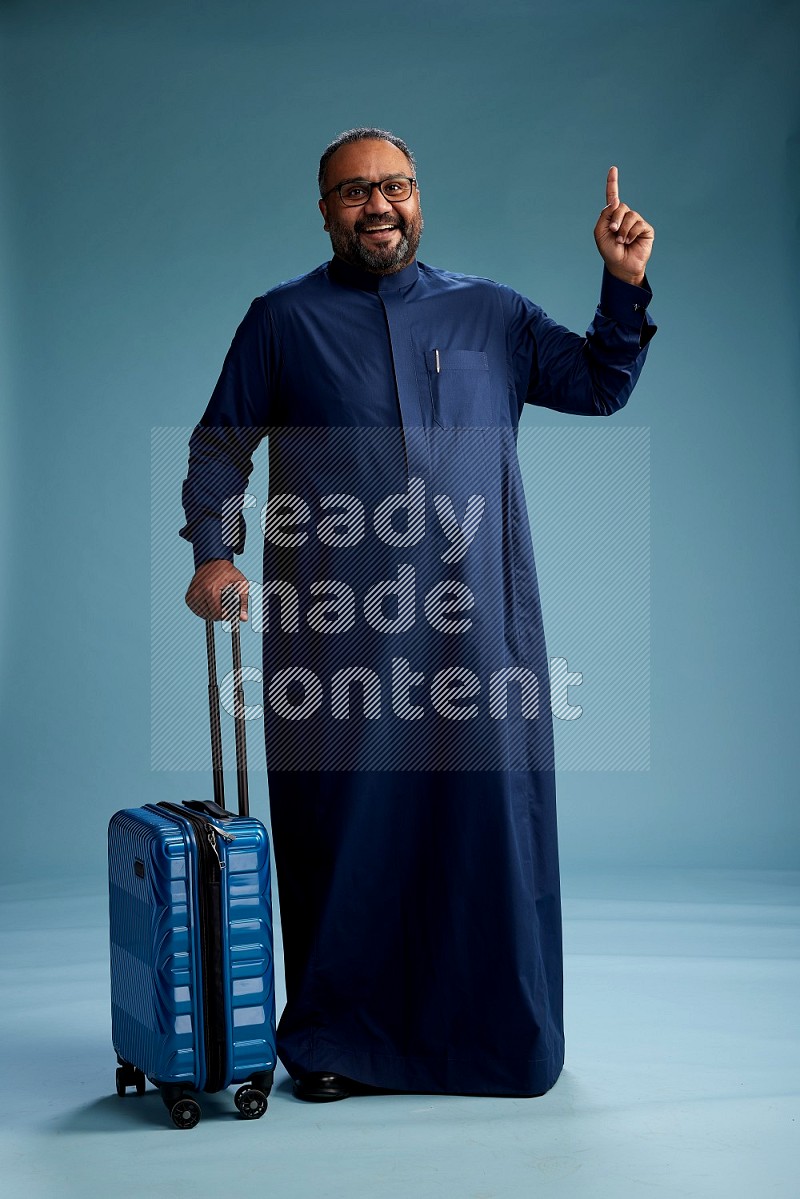 Saudi Man without shimag Standing pulling travel bag on blue background