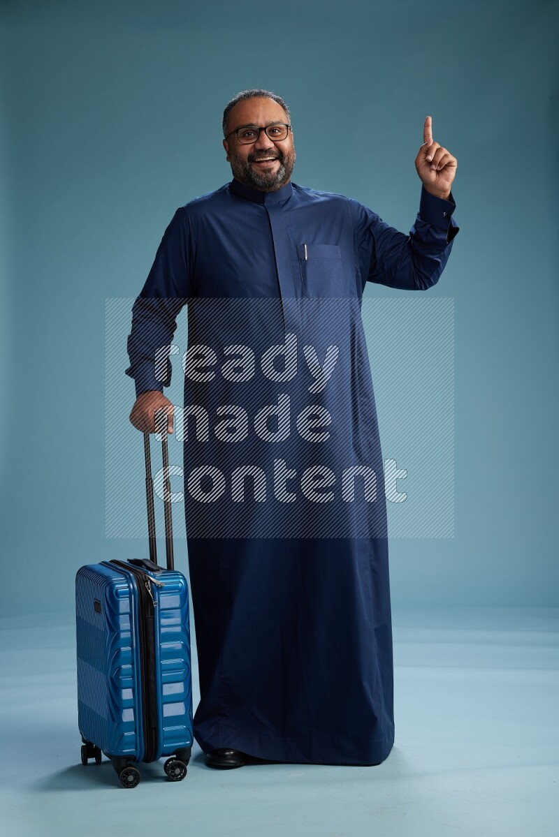 Saudi Man without shimag Standing pulling travel bag on blue background
