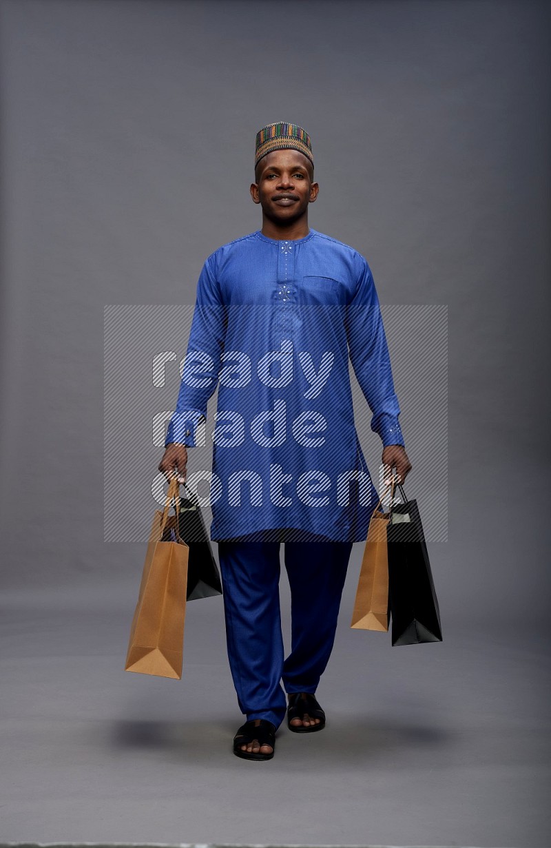 Man wearing Nigerian outfit standing holding shopping bag on gray background