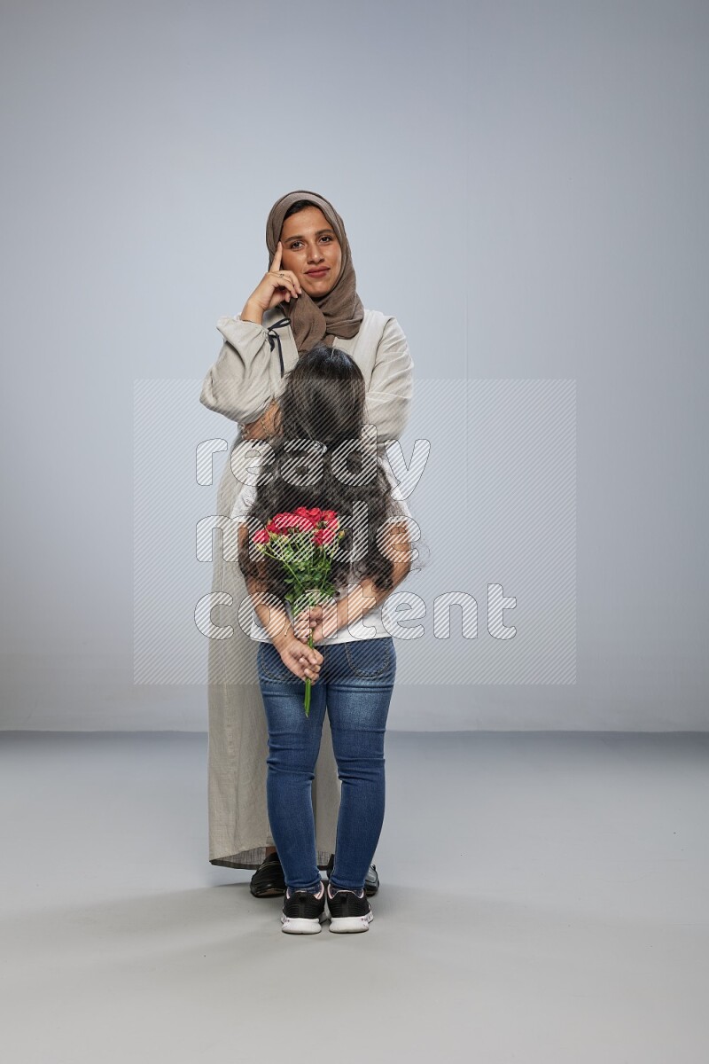 A girl hiding a flower behind her back for her mother on gray background