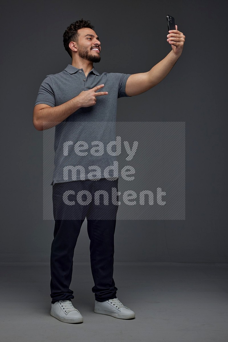 A man wearing casual and taking selfie with his phone different angles eye level on a gray background