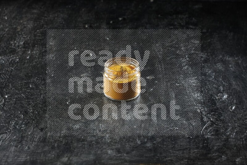 وعاء زجاجي ممتلئ ببودرة الكركم على خلفية سوداء