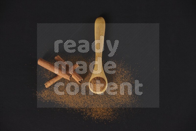 Cinnamon powder in a wooden spoon and cinnamon sticks beside it on black background