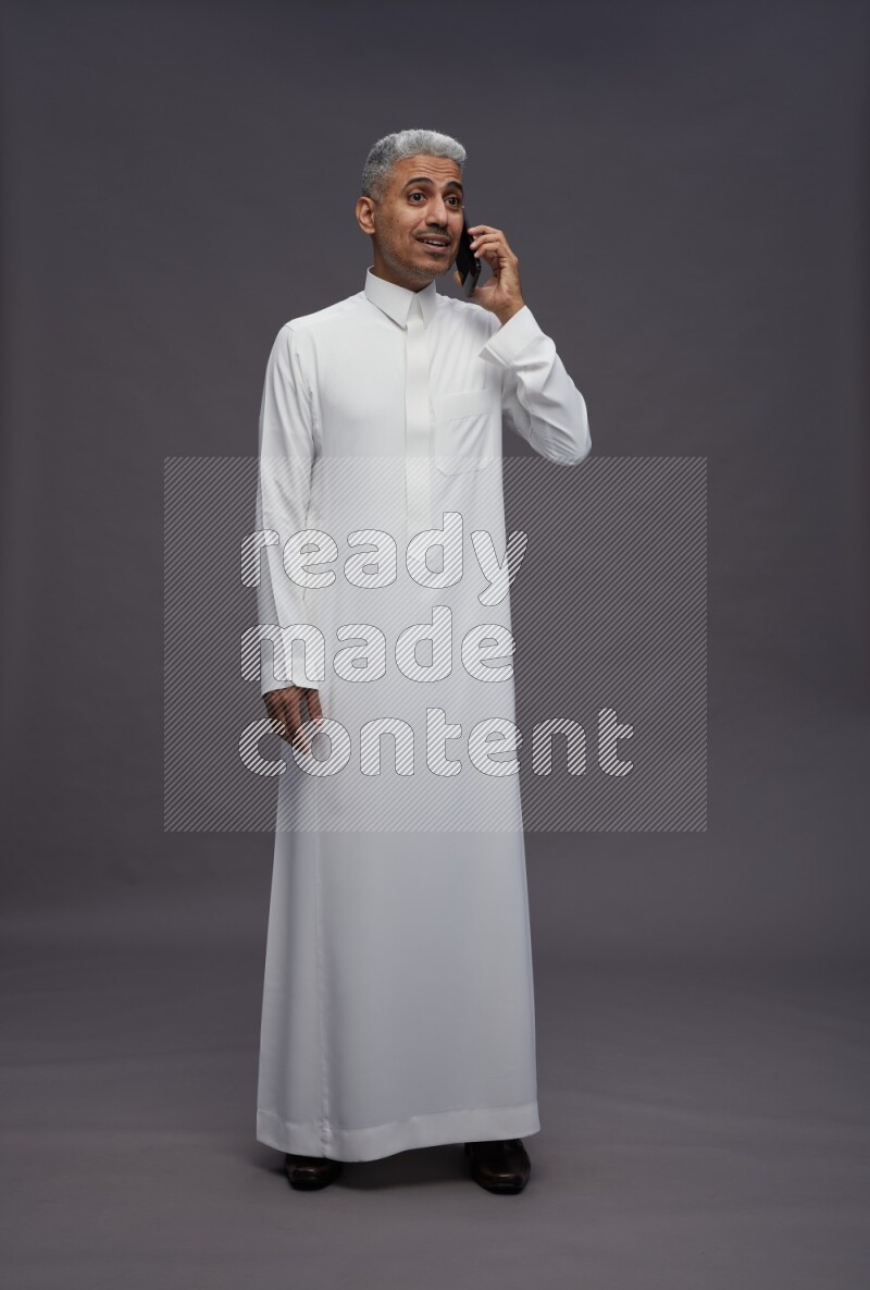 Saudi man wearing thob standing talking on phone on gray background