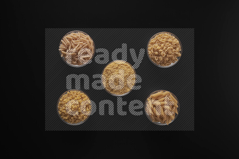 Different pasta types in 5 glass bowls on black background