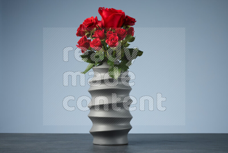An arrangement of vivid red roses in a grey spiral vase on black marble background