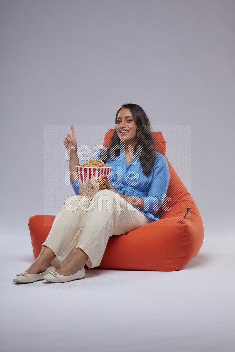 A woman sitting on an orange beanbag and eating popcorn