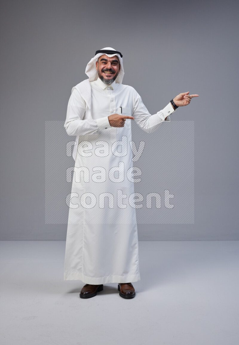 Saudi man Wearing Thob and white Shomag standing interacting with the camera on Gray background